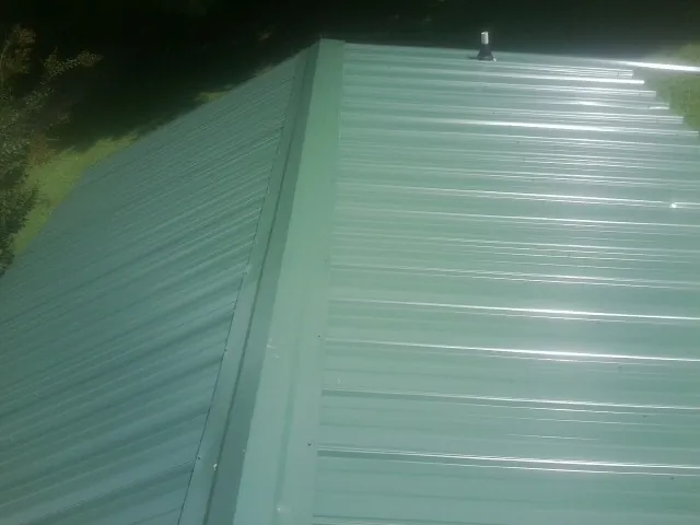 New green metal panels meeting at the ridge of a roof — Flat Roof Repair work by our crew in Baltimore