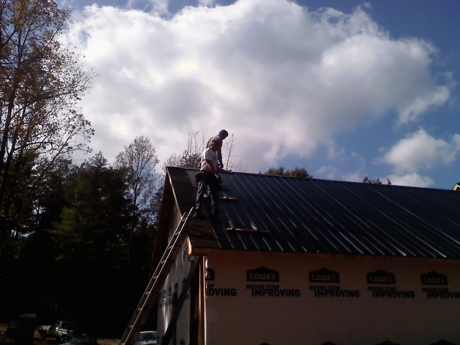 Roofer fastening dark metal panels high against a cloudy sky, from a Roof Inspection job in Baltimore